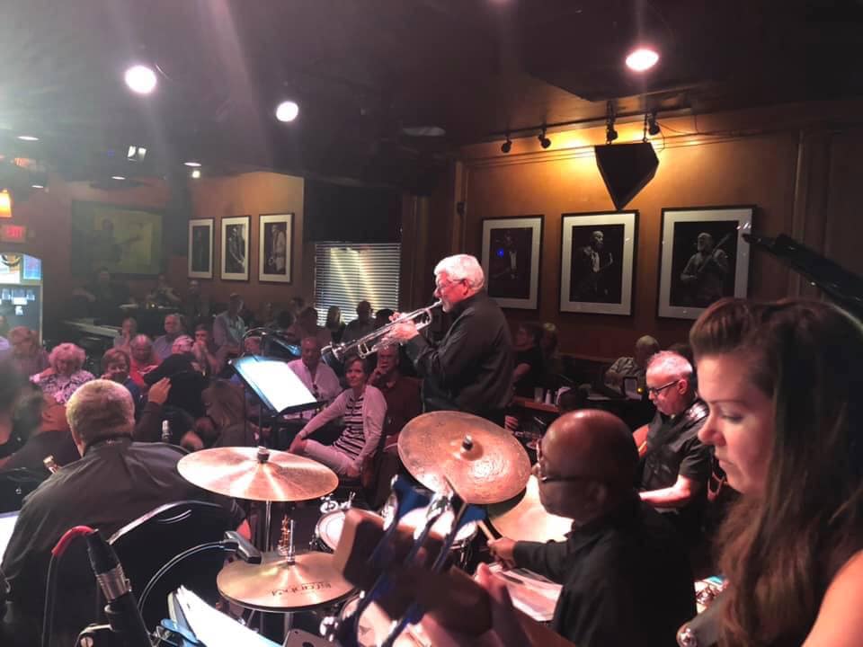 Joy Swing band performing on stage with a trumpet player in the center and a drummer behind