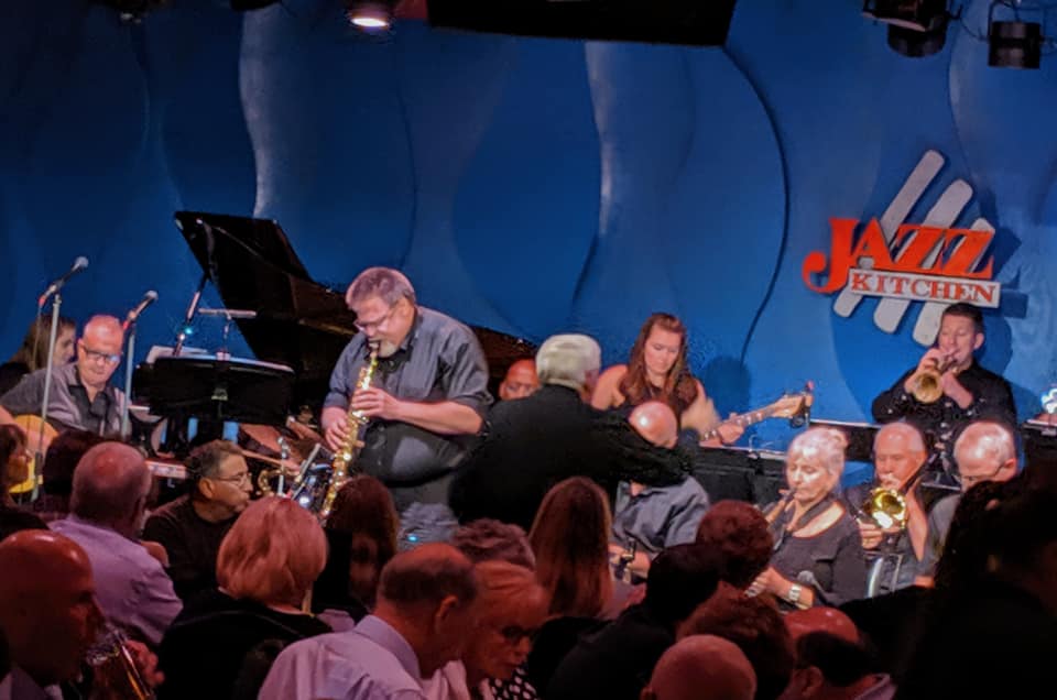 Joy Swing band performing on stage with a bright blue background featuring the Jazz Kitchen logo