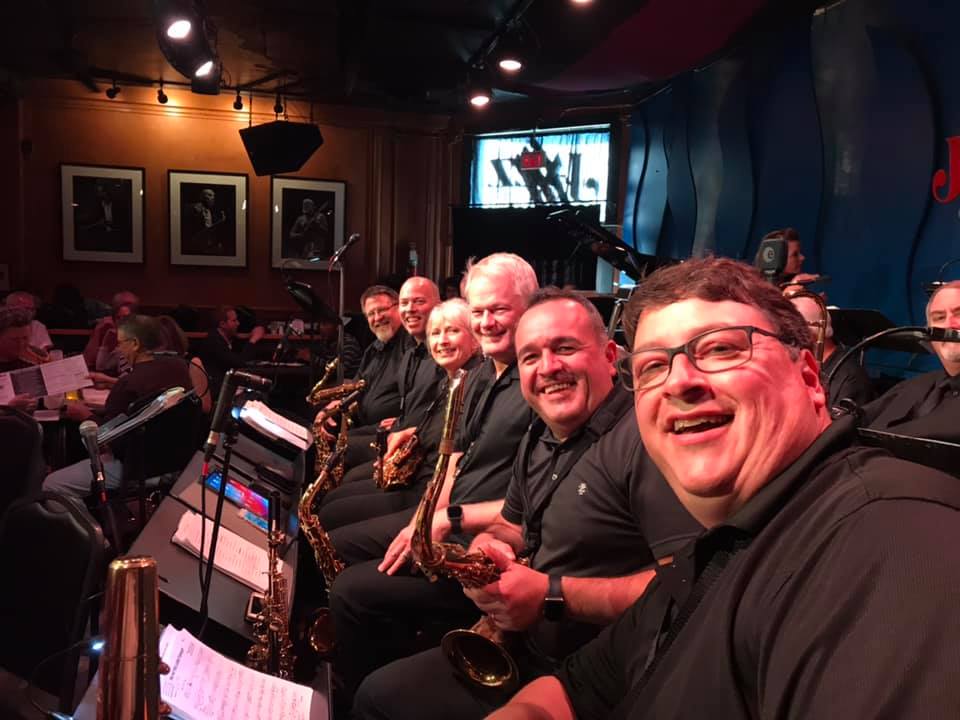 Group of musicians holding saxophones and smiling for a group photo while performing