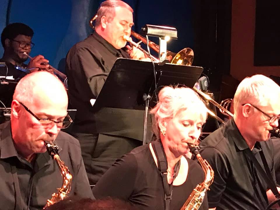 Jazz band performing on stage with saxophones in the foreground and a trombonist behind