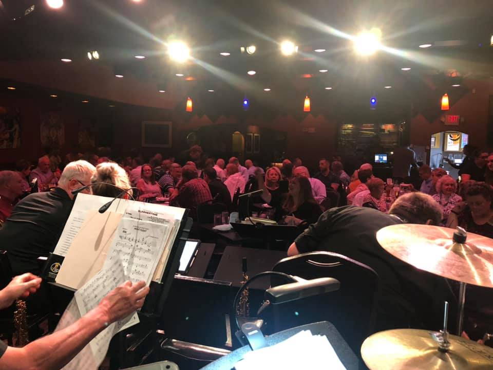 View from a jazz band looking out at an audience seated at tables in a dimly lit venue